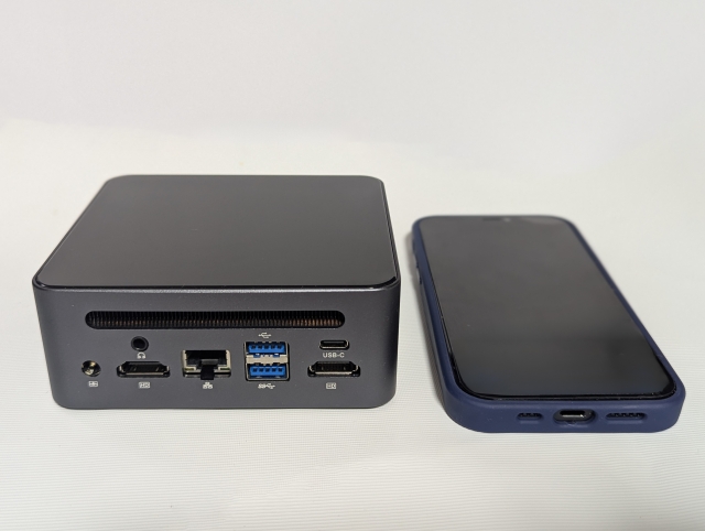 スマホと並べたミニPCの写真。小型で持ち運びやすく、省スペースで使えるサイズ感が伝わる