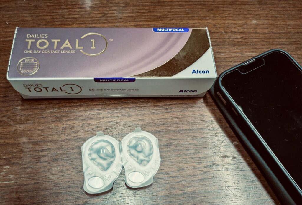 デイリーズトータルワンの箱のそばに黒いスマホの一部が映る写真。ネット購入をイメージした構図。