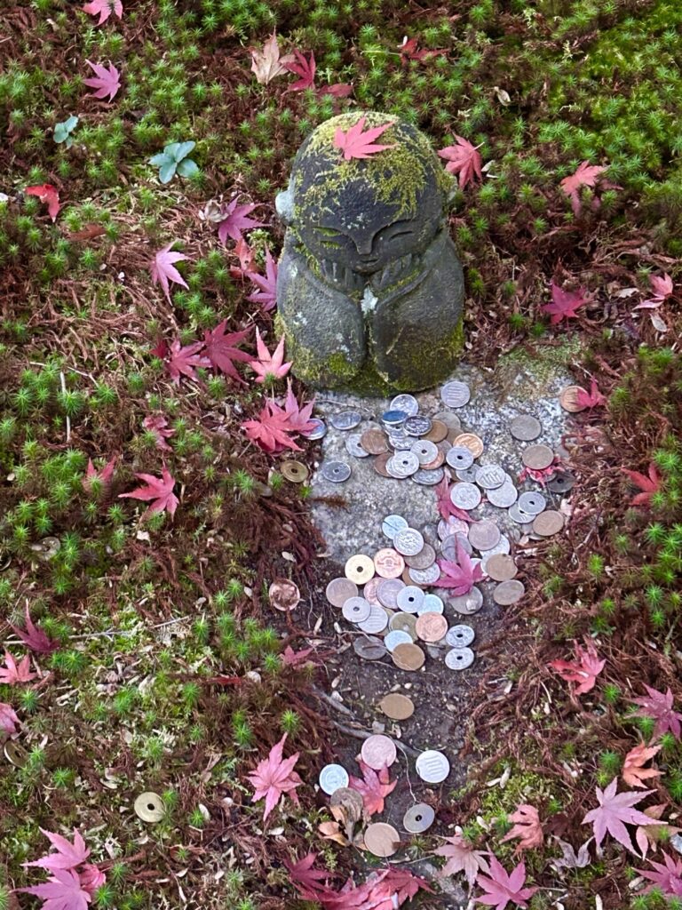 圓光寺の苔の上に佇む地蔵と、まわりに散った赤いもみじ。優しい表情の地蔵に秋の彩りが重なる、心が落ち着く風景。
