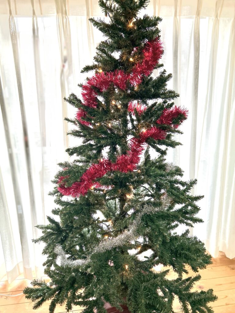 クリスマスツリーに赤とシルバーのガーランドを巻いている途中の様子。飾り付けのステップを説明するための写真。