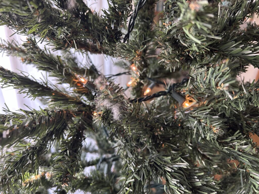 クリスマスツリーの枝にライトを奥から手前へジグザグに巻き付けている様子のクローズアップ写真。コードの配置が分かる。